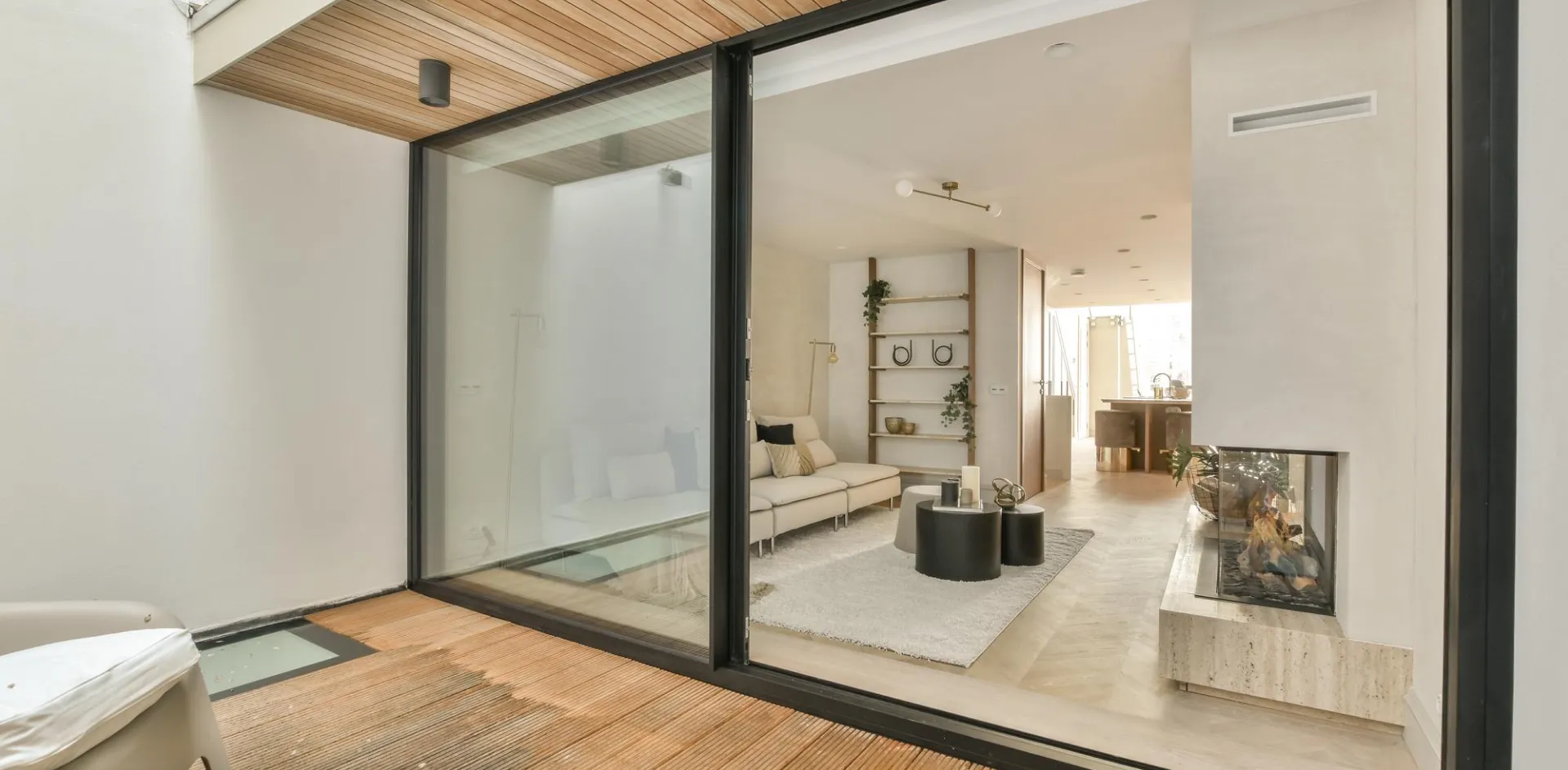 Black-framed aluminium sliding glass door open from a timber deck into a bright living room