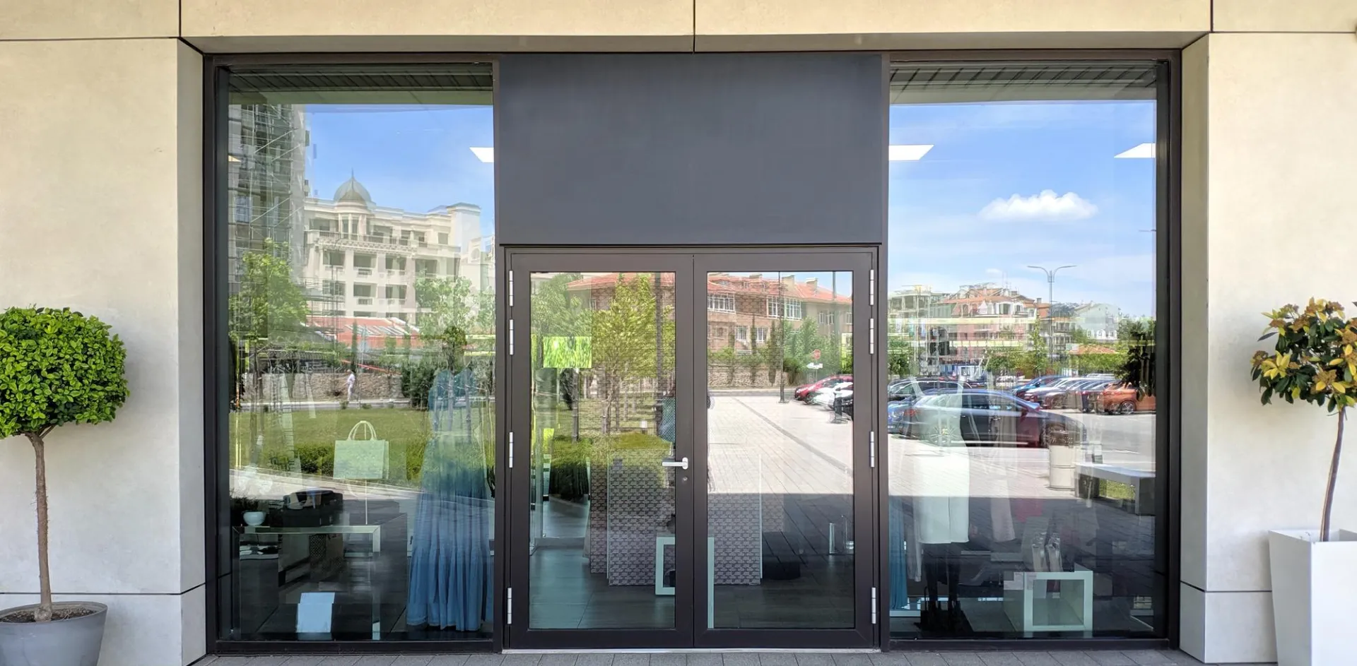 Dark aluminium framed glass shop front with double glass entry doors and a potted tree on either side