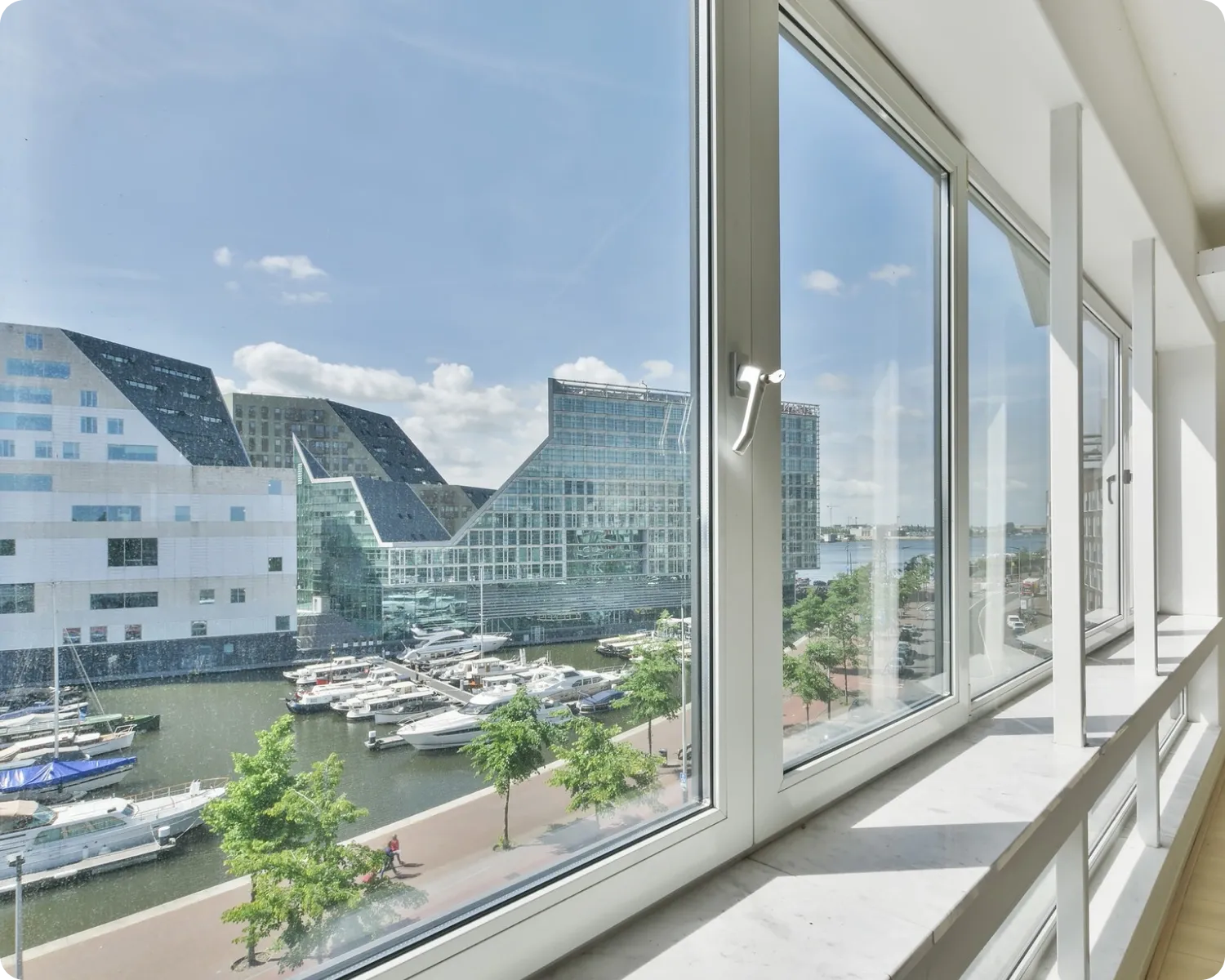 Floor-to-ceiling white aluminium framed windows with a lever handle looking out over a harbour and modern buildings