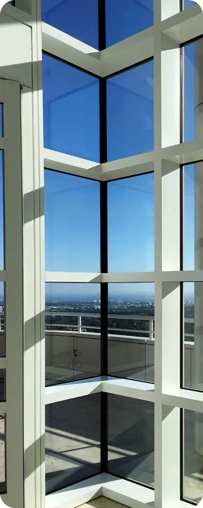 Corner glazing with slim white frames on a high floor, looking out over a city and a balcony