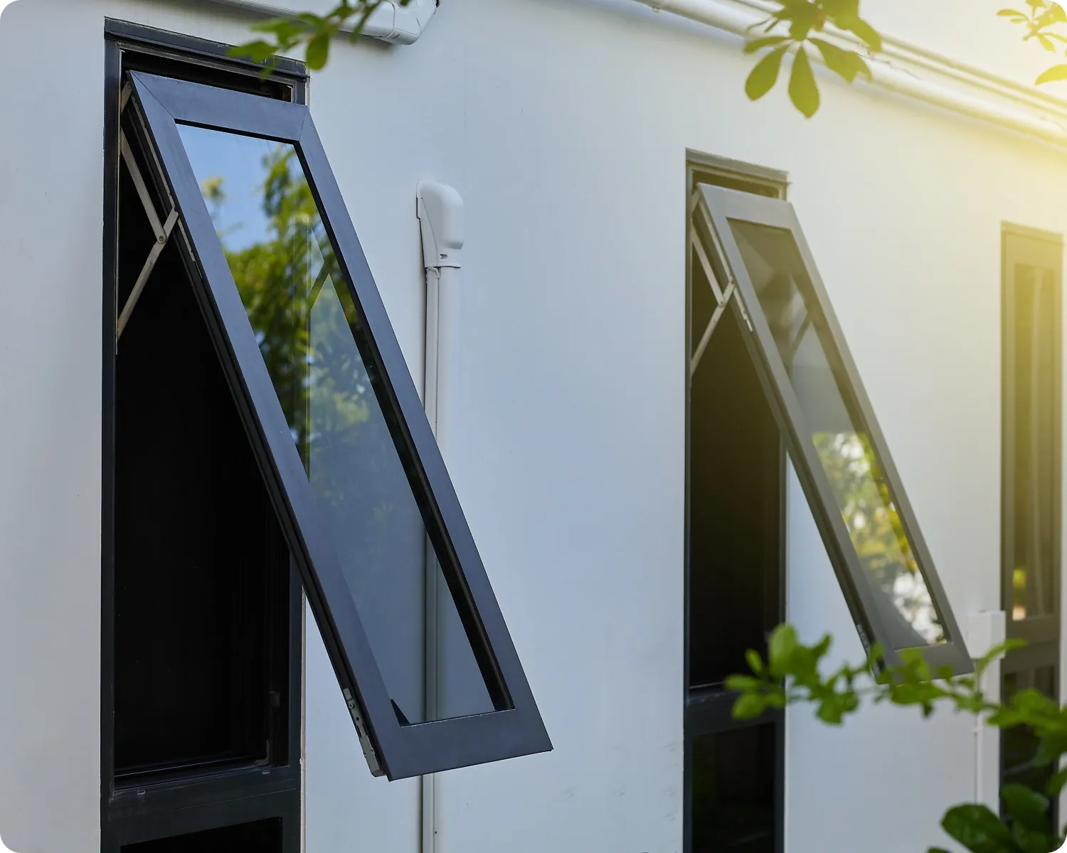 Two black aluminium awning windows propped open on a white rendered wall with greenery outside