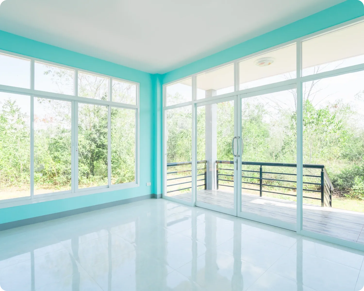 White aluminium sliding windows and a sliding glass door in a bright empty room opening onto a deck
