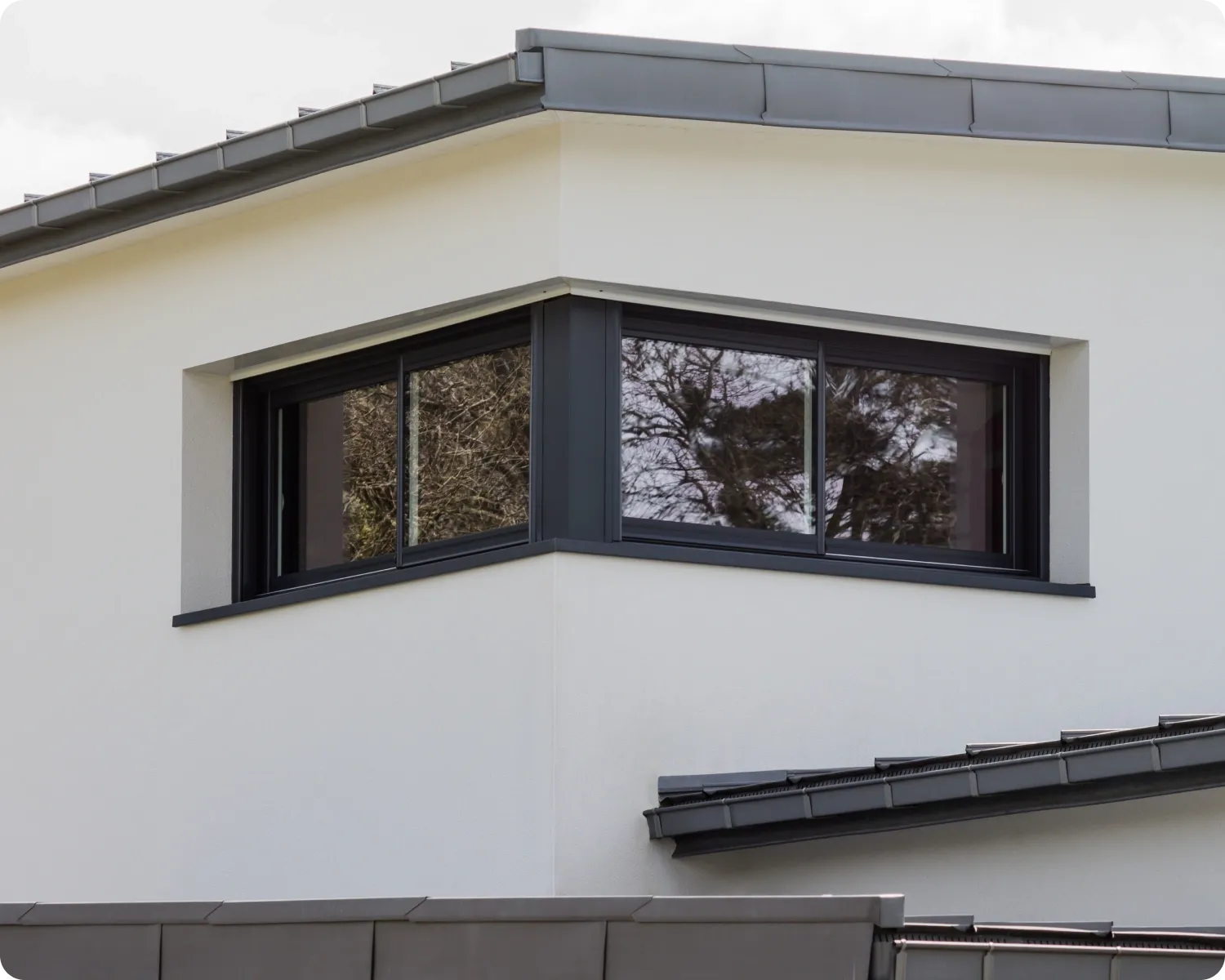 Black aluminium sliding windows wrapping the corner of a white rendered building with a flat roof