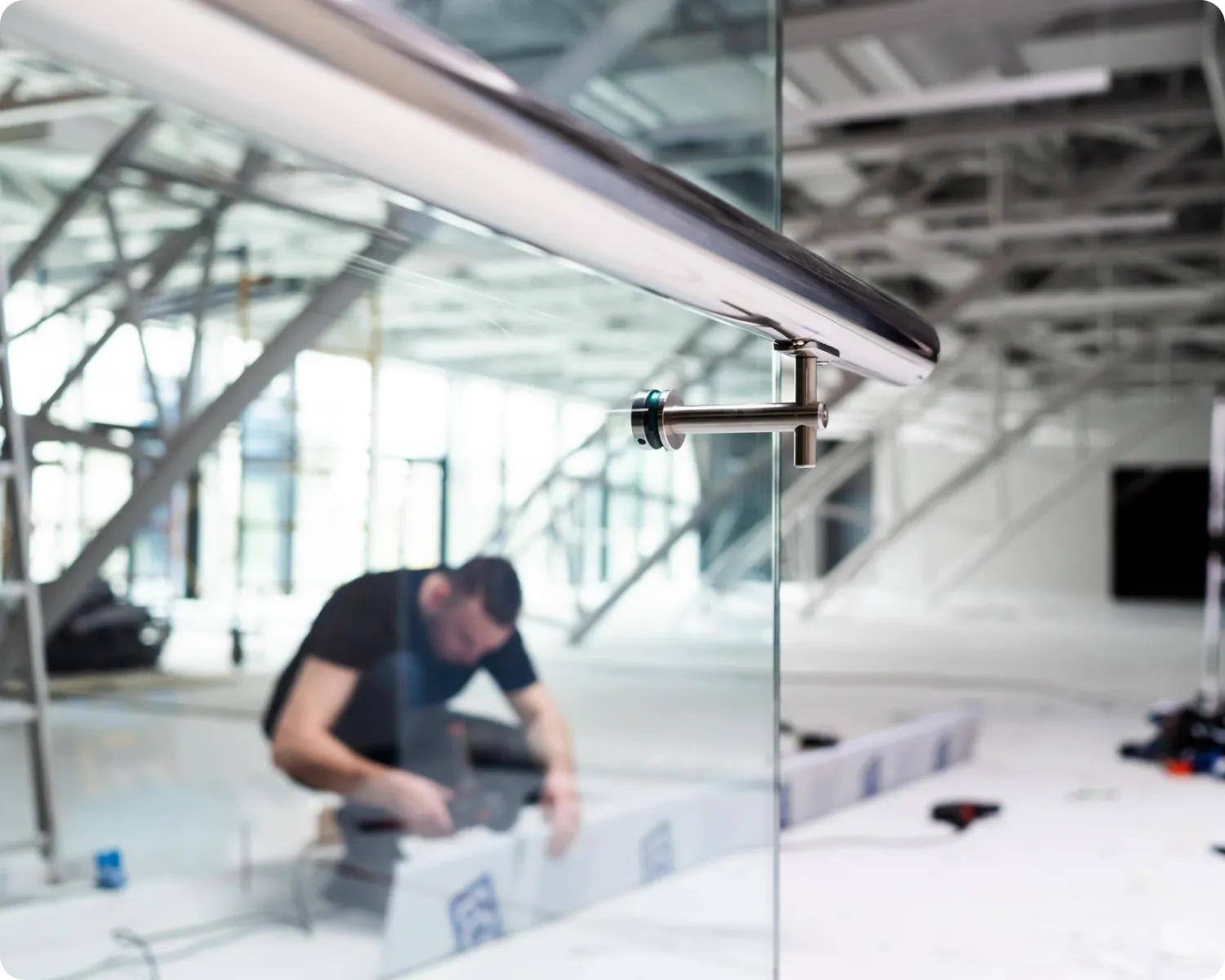Glass balustrade panel with a polished stainless steel handrail inside a commercial fit-out, with a tradesman working in the background