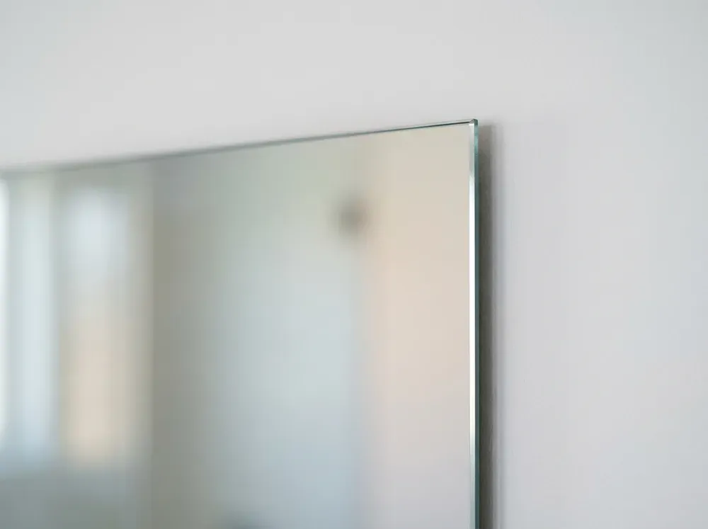 Corner of a frameless mirror with a flat polished edge on a white wall