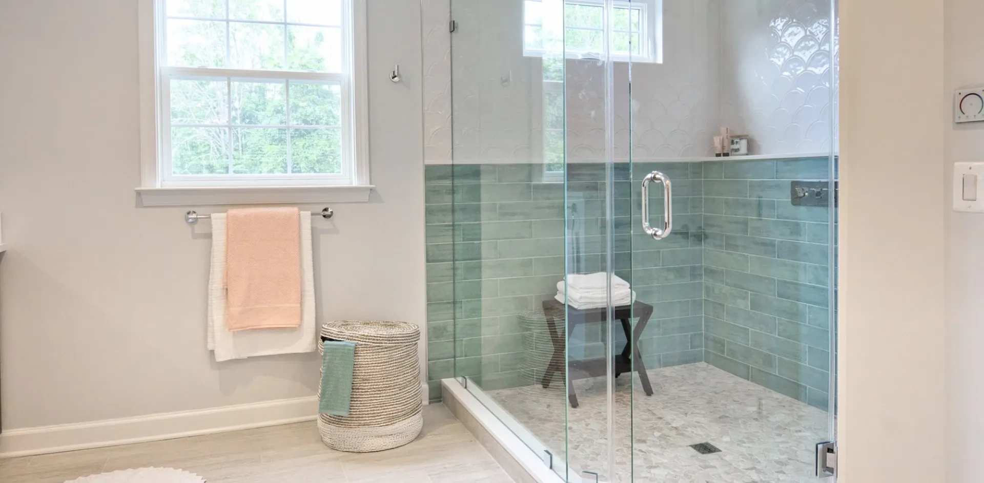 Frameless hinged glass shower screen with a chrome handle beside mint green subway tiles in a white bathroom