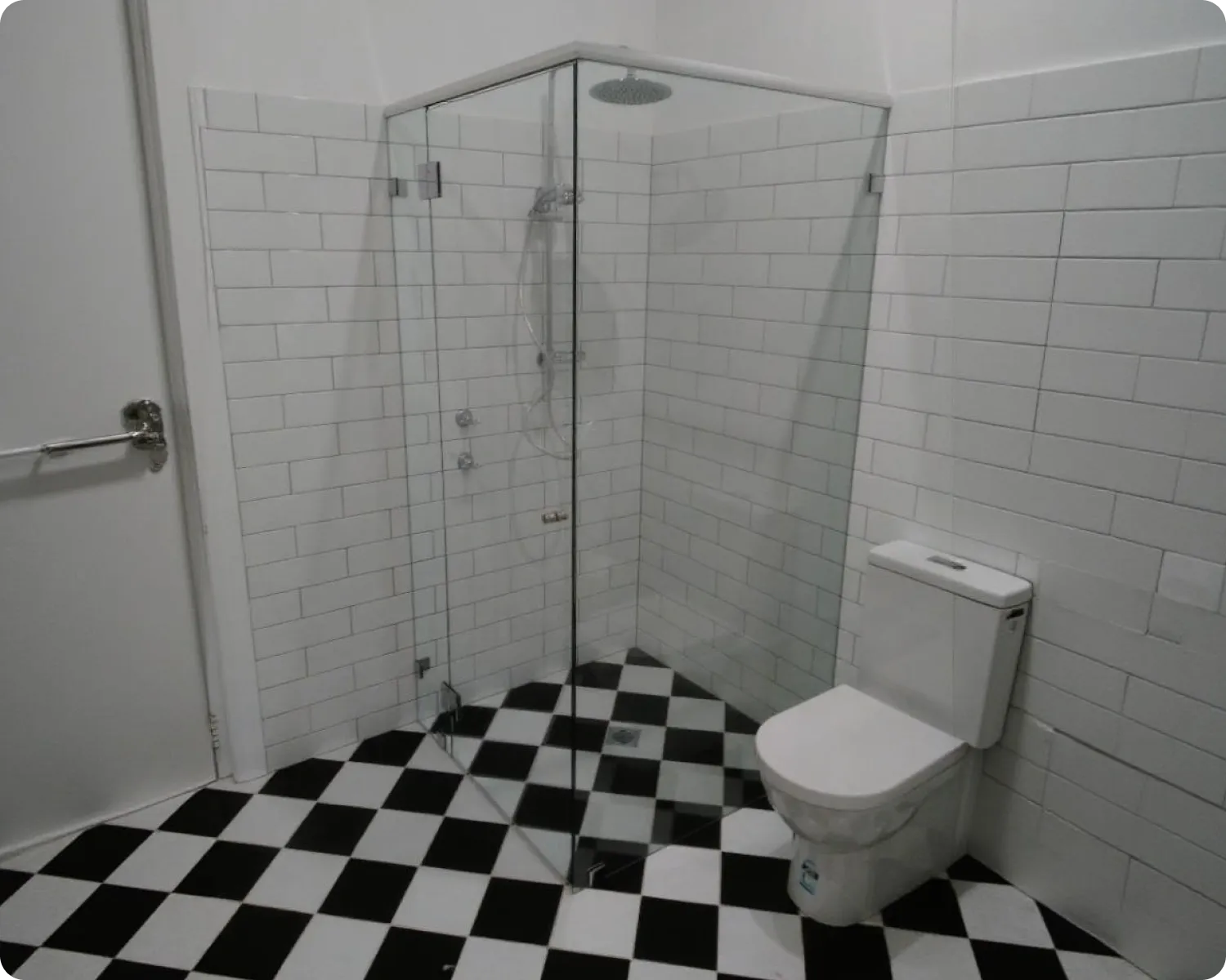 Frameless glass shower screen in a bathroom with white subway tiles and a black and white chequered floor
