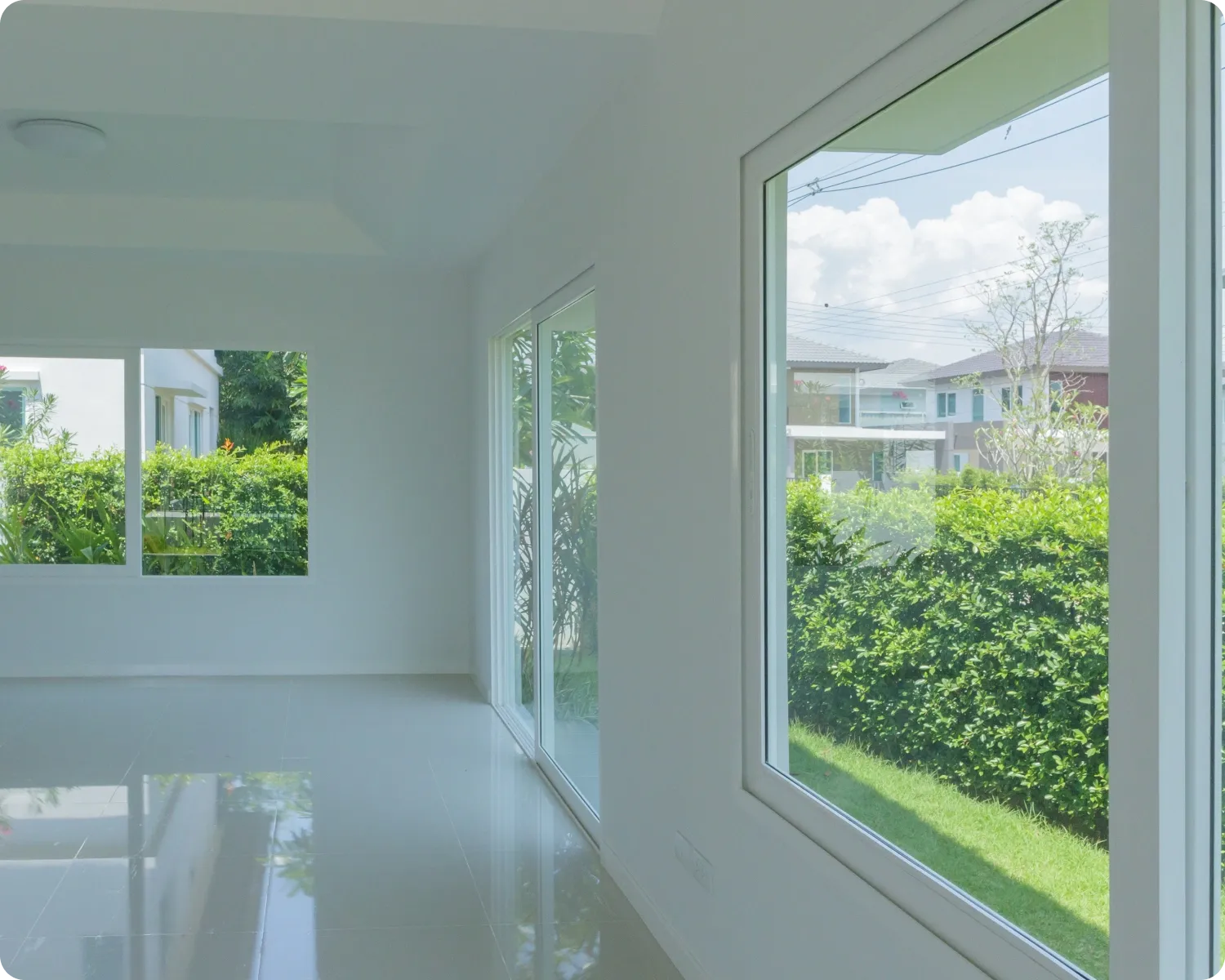 Bright empty room with new clear glass in large white-framed fixed windows and a sliding door, looking onto a hedge