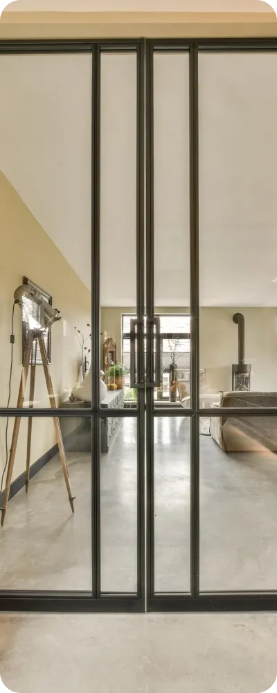 Black-framed hinged double glass doors looking through to a lounge room with a polished concrete floor