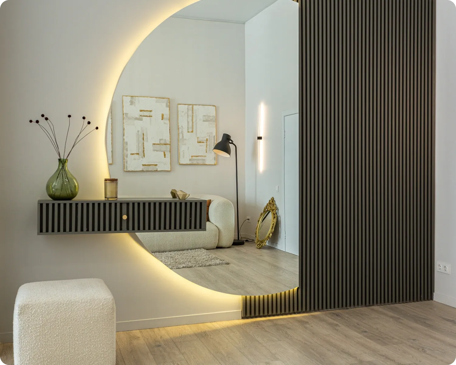 Large round backlit mirror on a hallway wall above a floating drawer, beside a timber slat panel