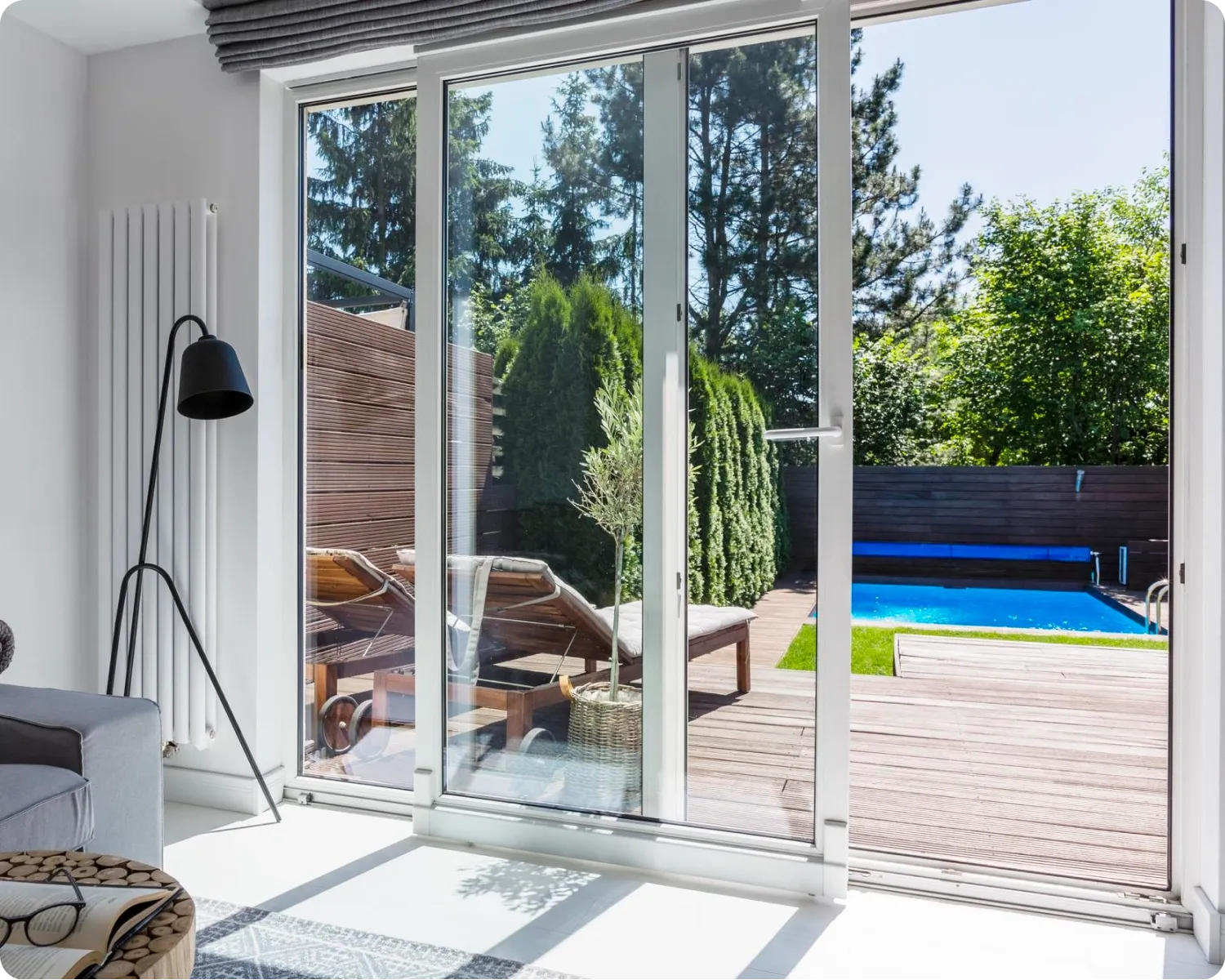White aluminium sliding door open from a living room onto a timber deck and swimming pool