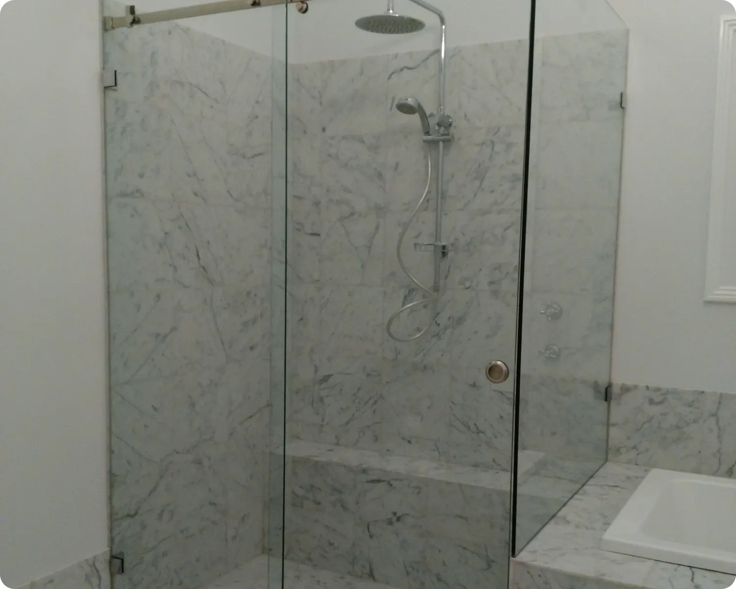 Frameless sliding shower screen with a slim top rail in a marble tiled bathroom next to a bath