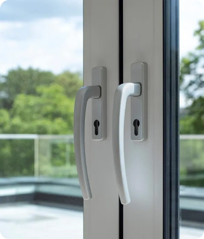Close-up of two white aluminium door handles with key locks on a glass door, with a balcony and trees behind
